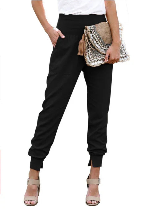 woman wearing black tapered jogger pants with cuffed ankles, white top, and nude heeled sandals, holding embellished clutch bag