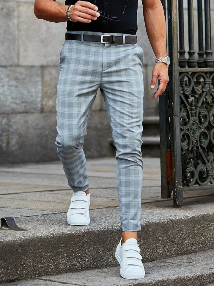 Man wearing gray plaid pants, black belt, white sneakers, and black shirt walking on stone steps