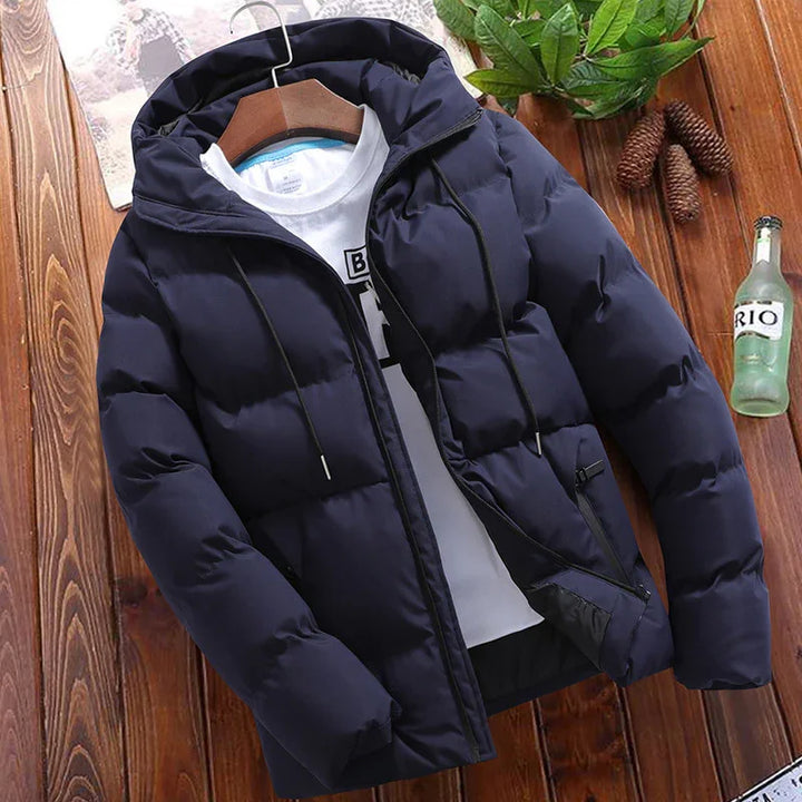 Navy blue puffer jacket with hood and black zipper, displayed over white graphic T-shirt on wooden floor