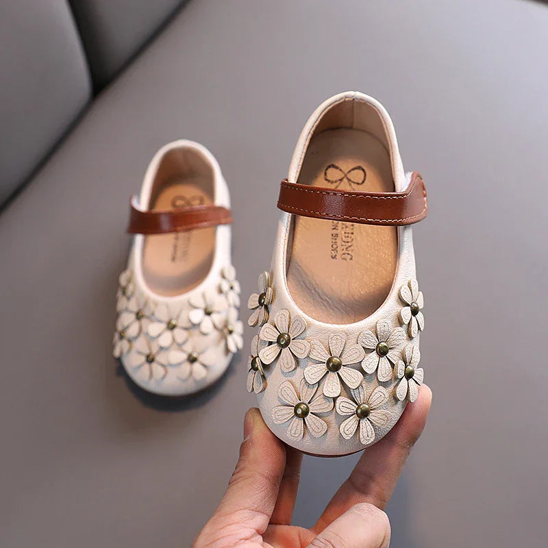 White baby shoes with brown straps and decorative flower appliques displayed on gray background