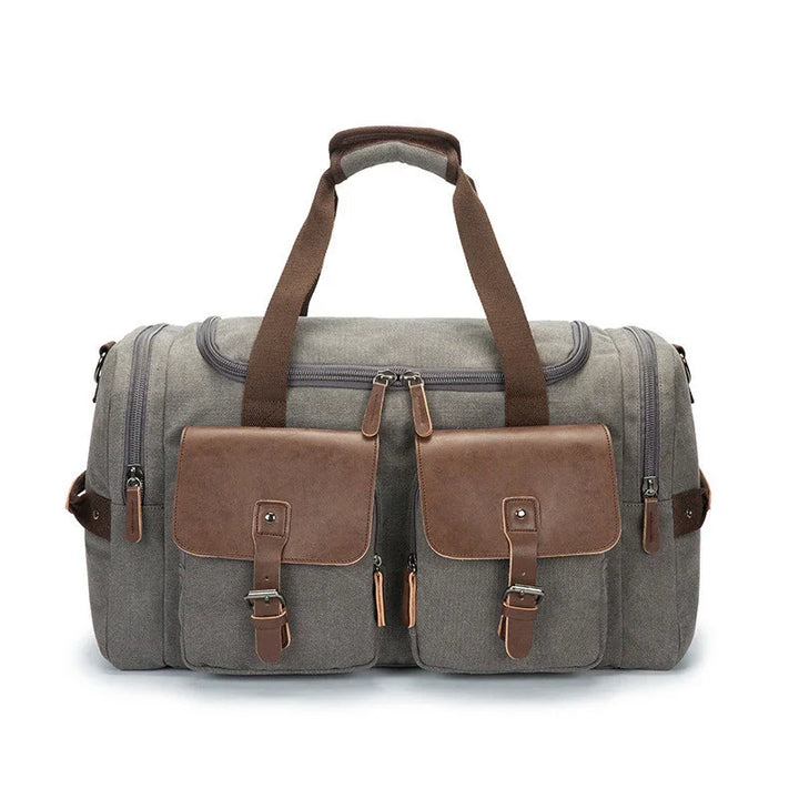Gray canvas duffel bag with brown leather pockets and handles, multiple zippered compartments