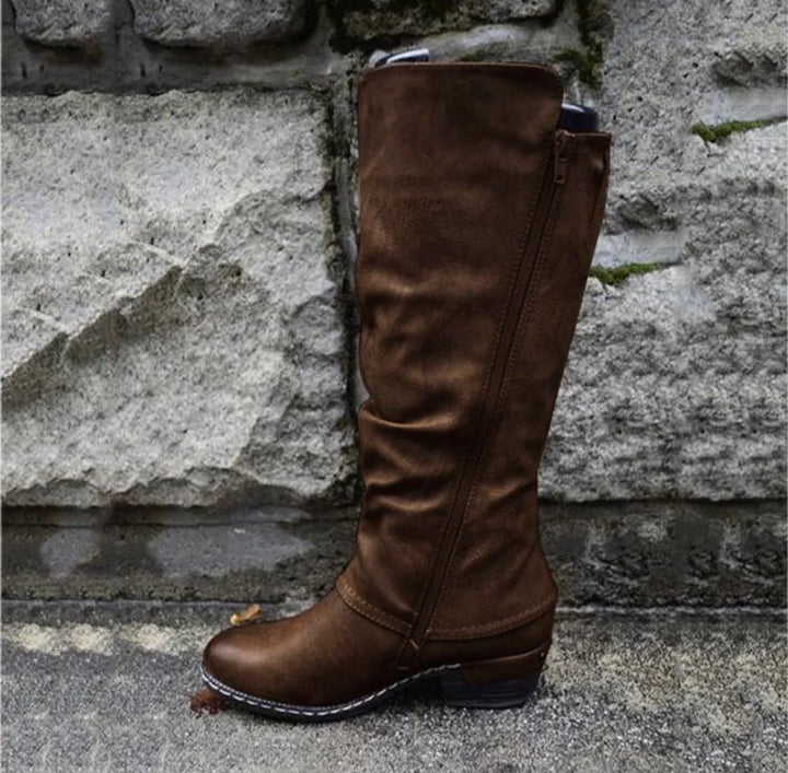 brown knee-high leather boot with side zipper against stone wall background