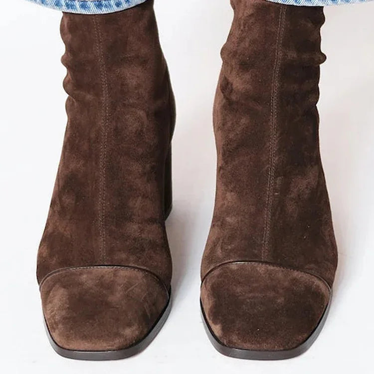 Close-up of brown suede square-toe ankle boots worn with blue jeans on white background