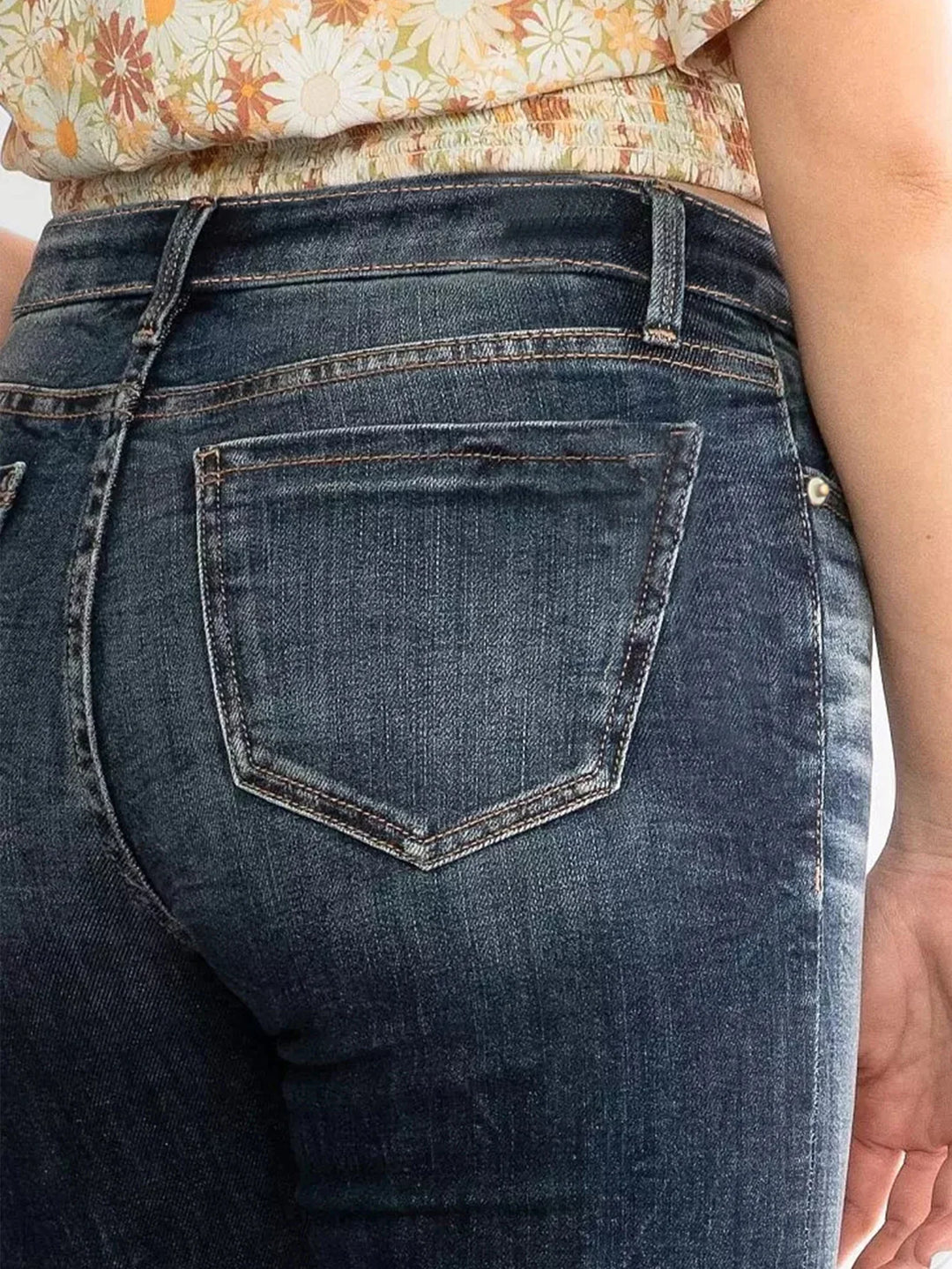 Close-up of woman wearing dark blue denim jeans and floral crop top showing back pocket details