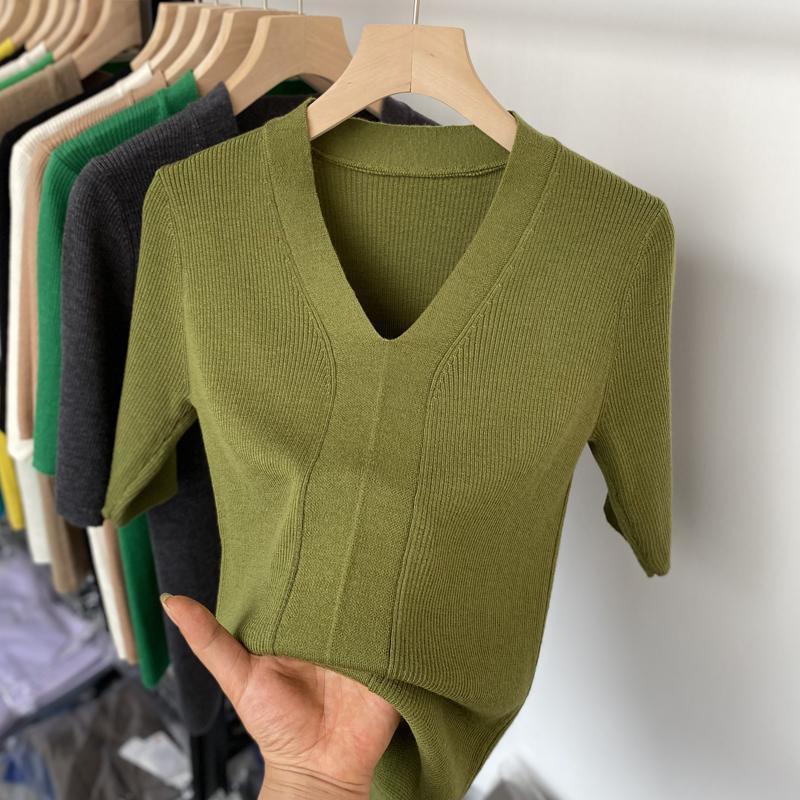 Hand holding olive green ribbed knit V-neck short sleeve sweater on wooden hanger with assorted sweaters in background