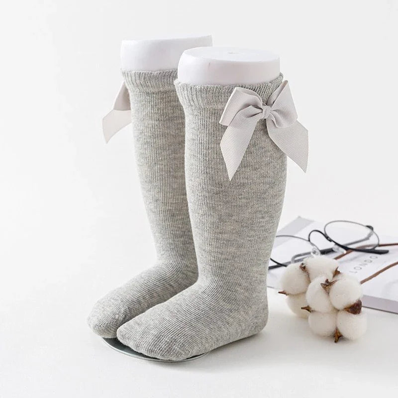 Pair of grey knee-high knit socks with large decorative bows on white mannequin feet