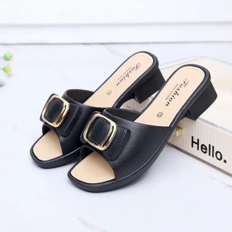 Black open-toe block heel sandals with gold buckle detail on white surface next to a box labeled Hello