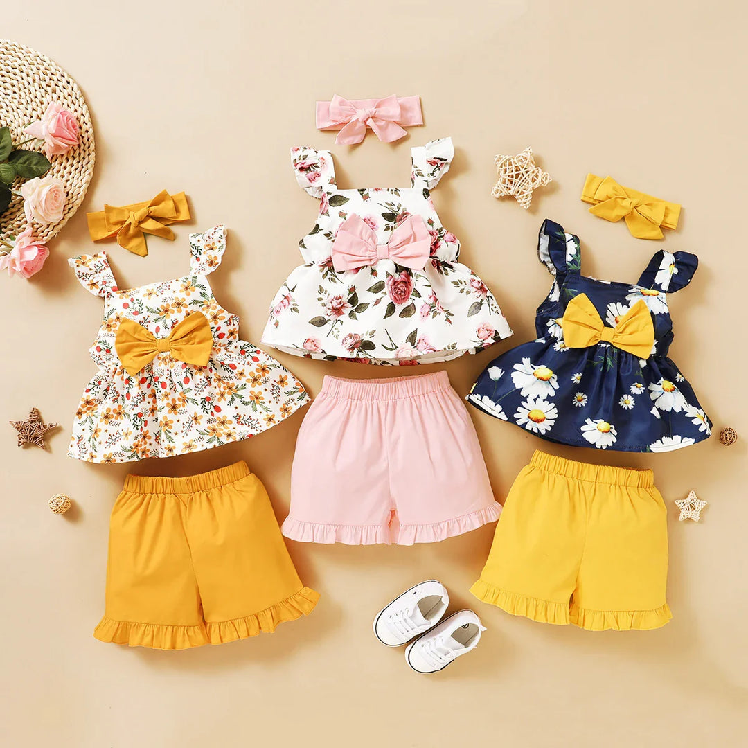 Three floral baby girl outfits with bows, matching shorts, headbands, and white shoes on beige