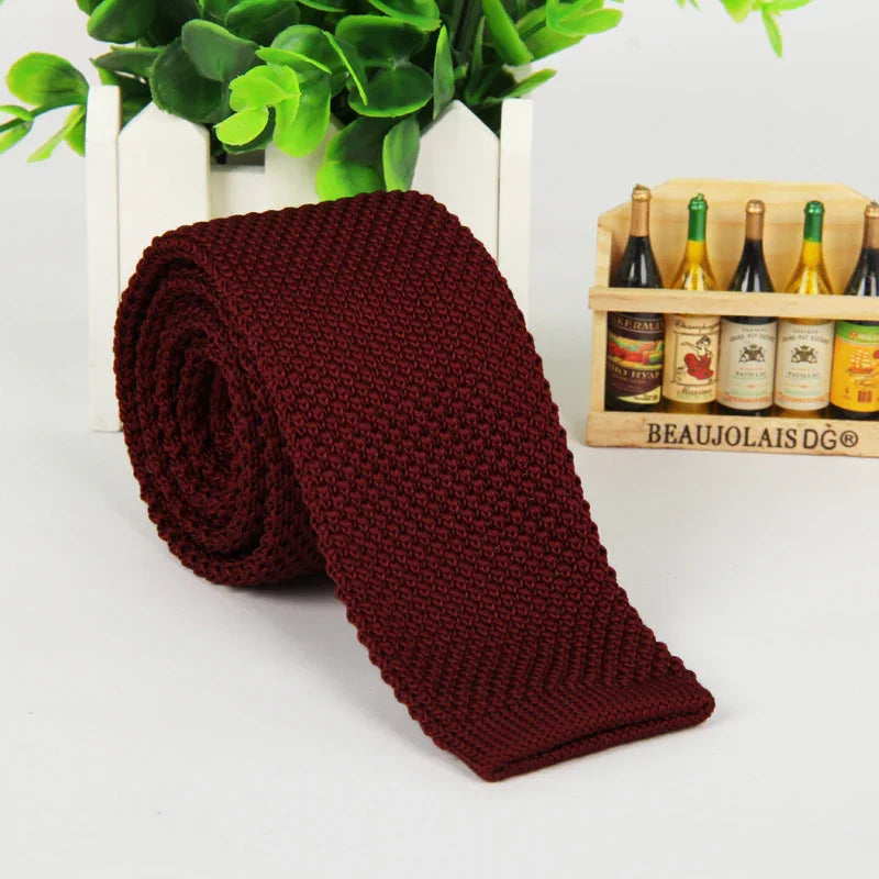 Rolled burgundy knit tie on white surface with green plant and wooden wine bottle crate