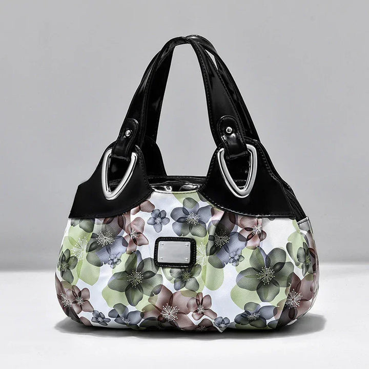 Stylish handbag with black leather handles and multicolor floral fabric body against gray background