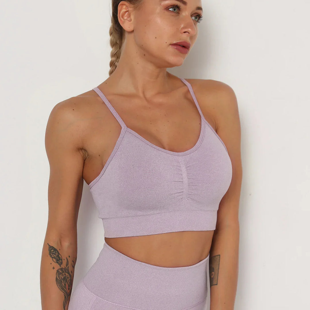 woman in lavender sports bra and high-waist leggings with braided hair and tattoos against white background