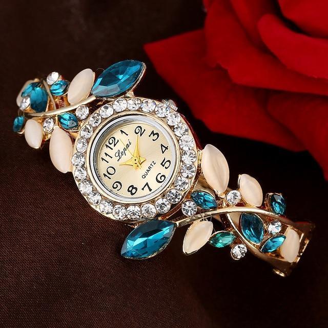 Elegant gold wristwatch with crystal-studded bezel and blue leaf-shaped gemstones on floral bracelet