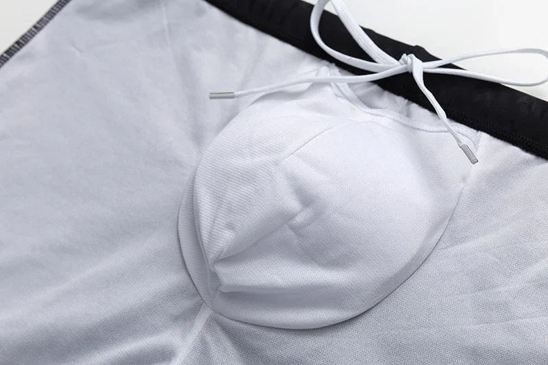 Close-up of white swim trunks with black waistband and white drawstring on a light surface