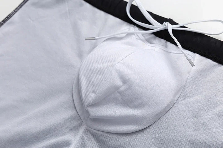 Close-up of white swim trunks with black waistband and white drawstring on a light surface