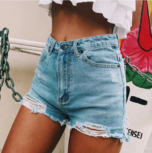 Close-up of a woman wearing light blue distressed denim shorts and a white ruffled crop top