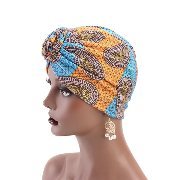 Side profile of mannequin wearing orange and blue patterned African print headwrap with gold and pearl dangle earring