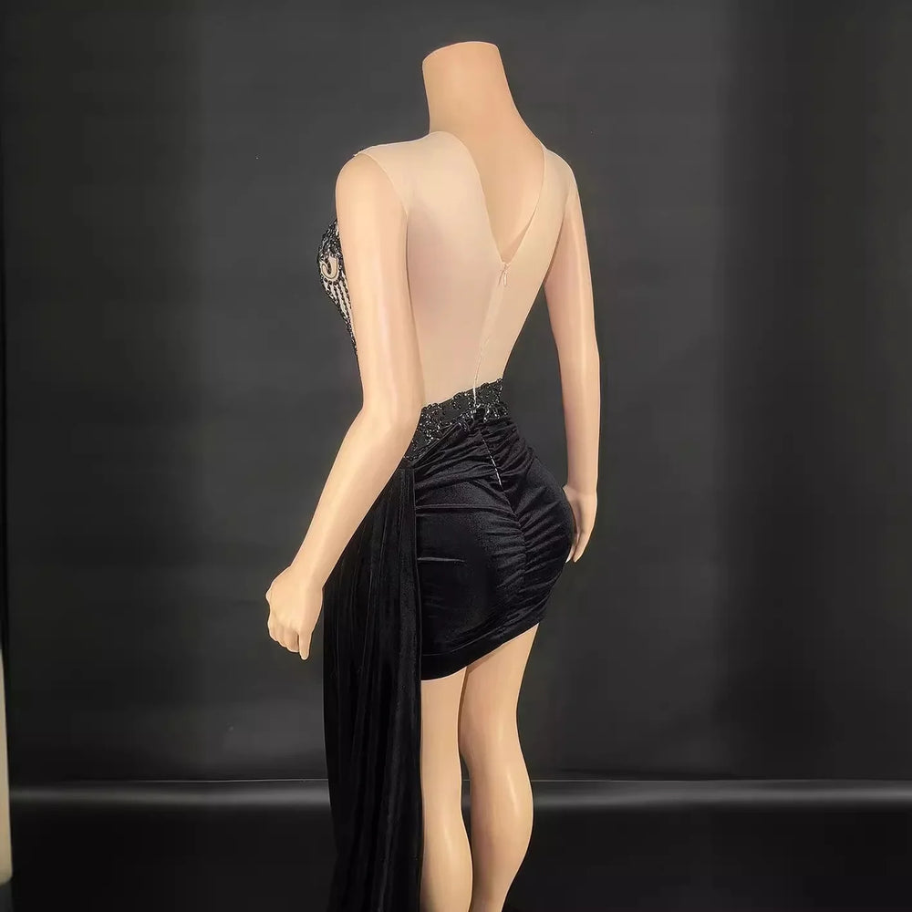 Back view of a sheer sleeveless black mini dress on mannequin with beaded waist and draped fabric detail