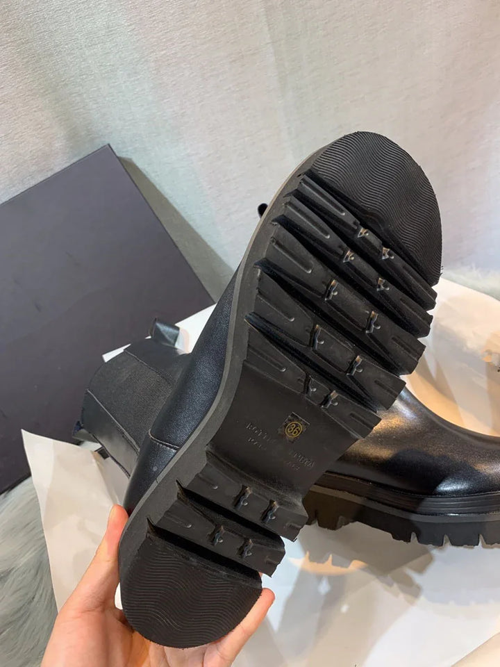 Close-up of black leather boots with chunky rubber sole and tread pattern, held in hand