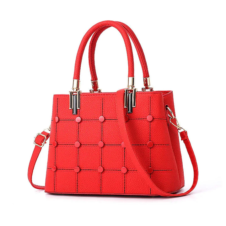 Red textured leather handbag with grid pattern, round studs, dual top handles, and detachable shoulder strap
