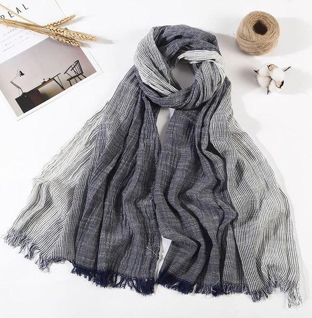 Gray and white striped lightweight scarf with fringed edges displayed on white surface with cotton, twine, and photo