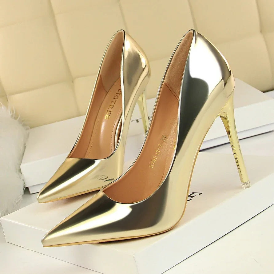 Pair of shiny gold high heel pointed-toe pumps on white box in elegant setting