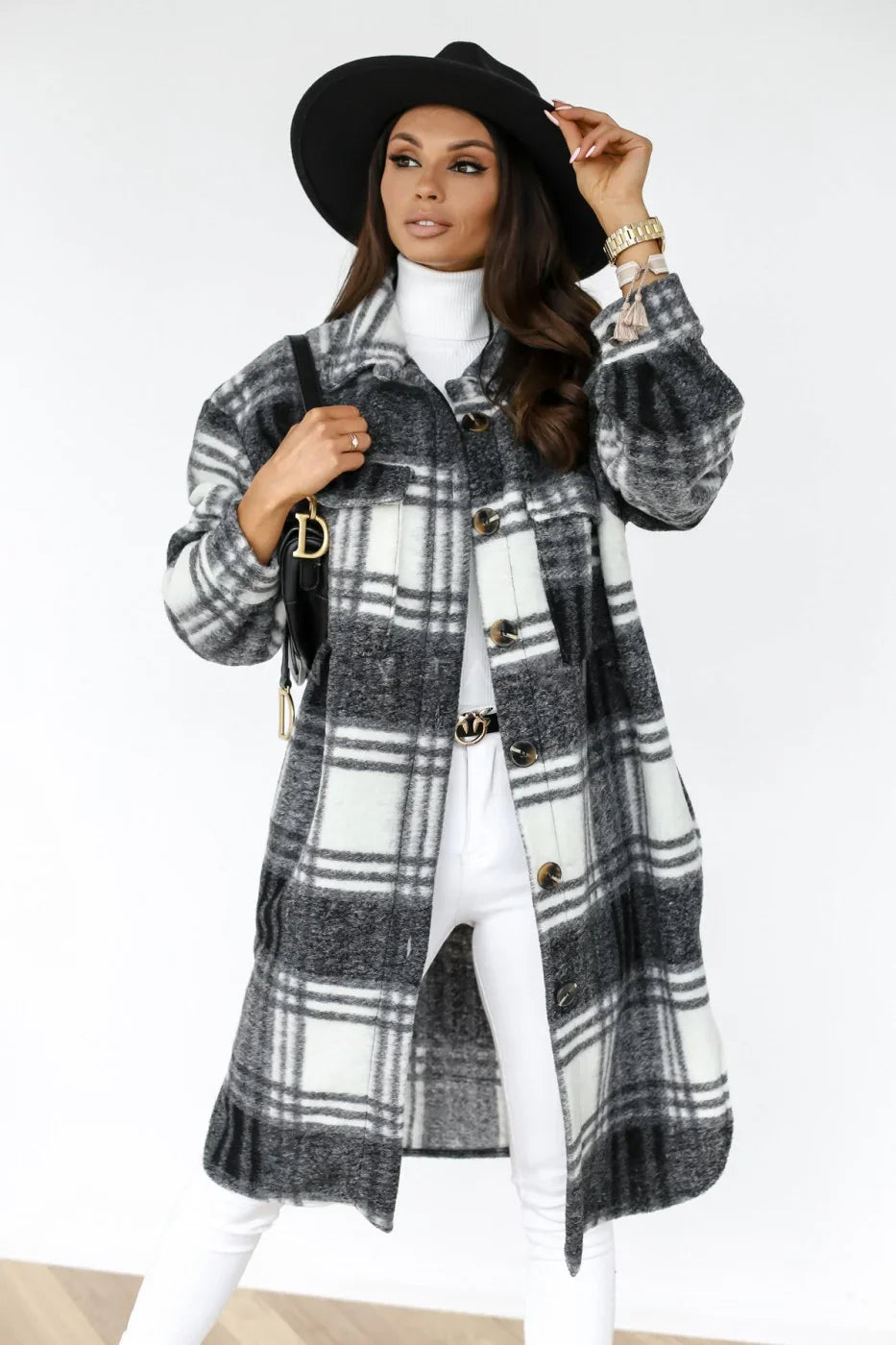 Woman wearing black and white plaid long coat, black wide-brim hat, white turtleneck, and white pants