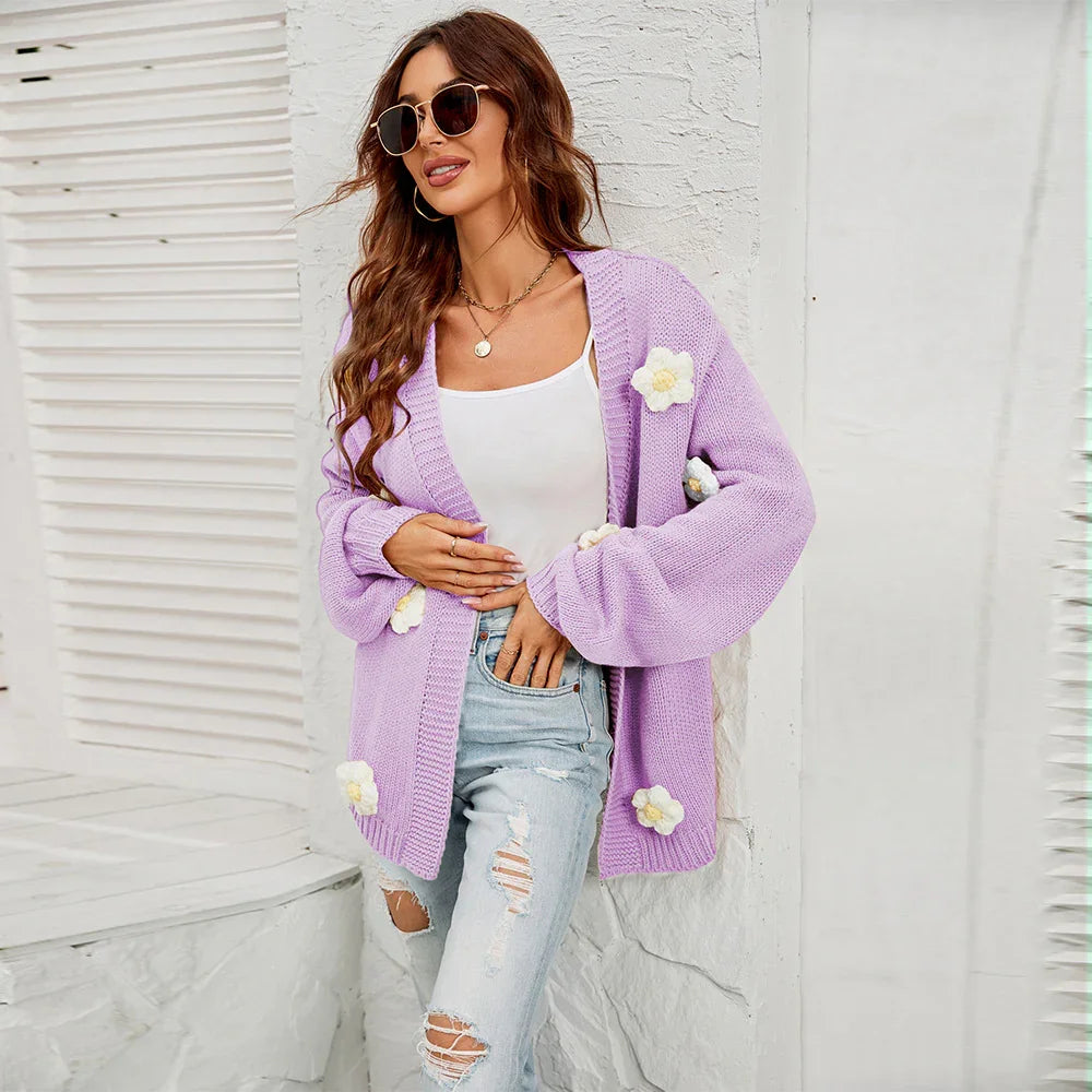 Woman wearing lilac knitted cardigan with white floral appliques, white tank top, and ripped jeans