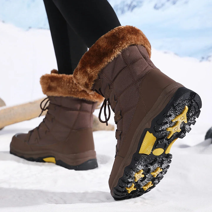 Pair of brown winter snow boots with fur lining and rugged yellow-soled tread walking in snow