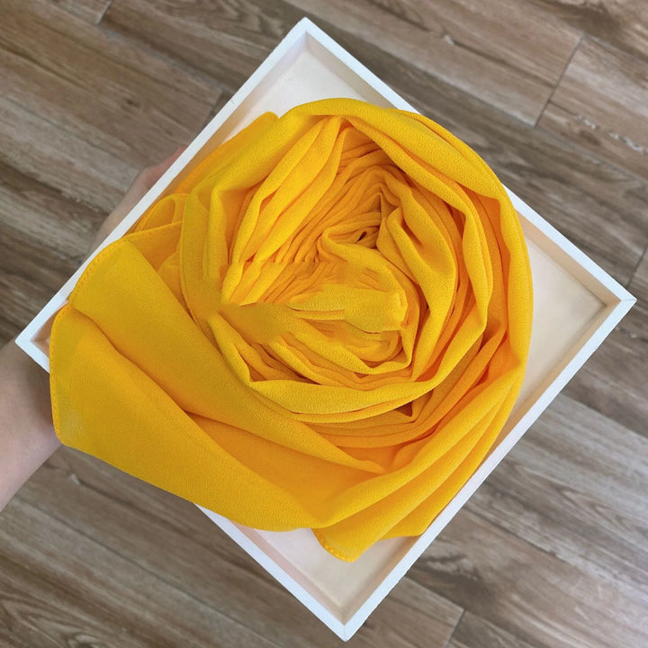 Hand holding white box with neatly folded vibrant yellow fabric on wooden floor