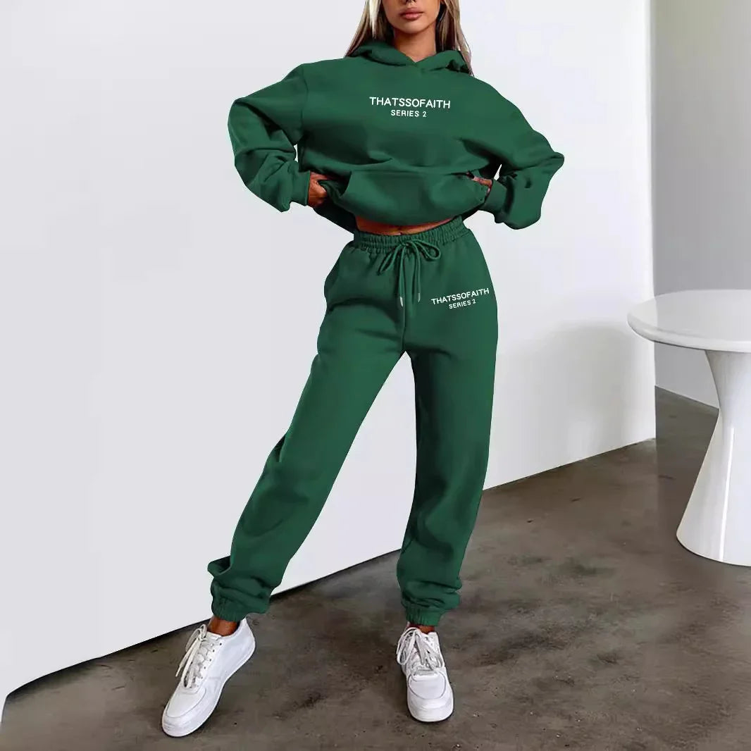 Woman wearing dark green Thatssofaith Series 2 hoodie and joggers with white sneakers indoors