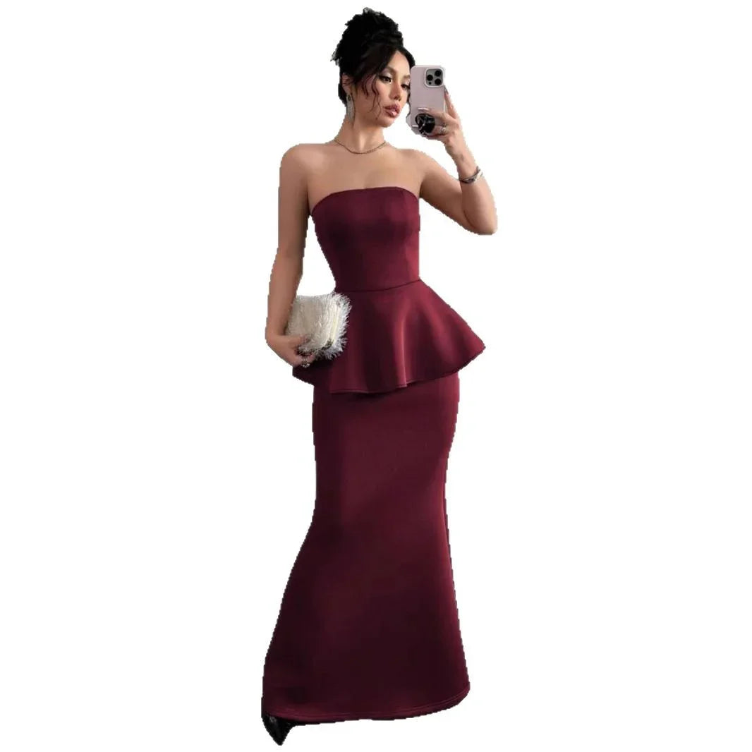 Woman in a strapless burgundy peplum evening gown holding a white clutch and taking a selfie
