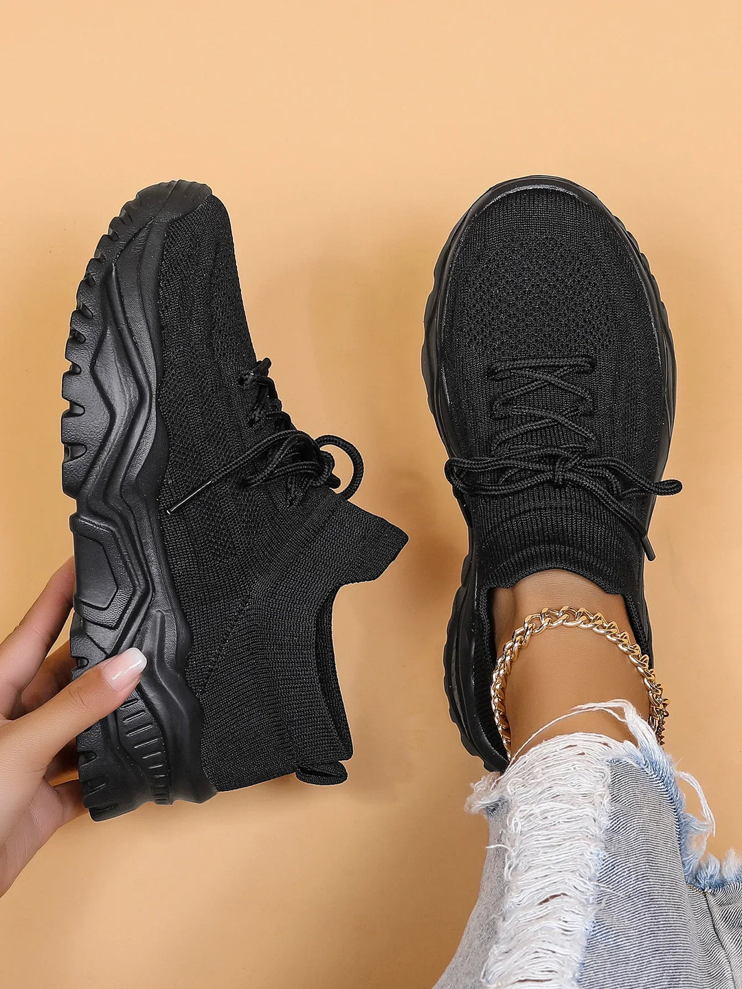Black knitted chunky sneakers with thick textured sole, worn with distressed jeans and gold ankle bracelet