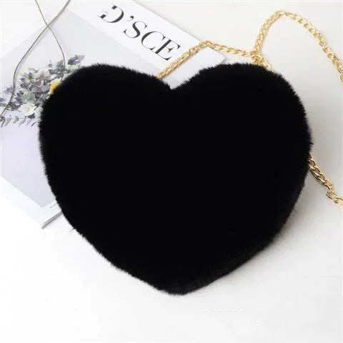 Black heart-shaped fuzzy purse with gold chain strap on white surface with magazine