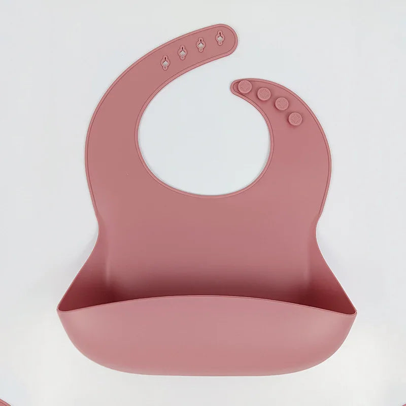 silicone baby bib in muted pink with adjustable button snaps and food catcher pocket