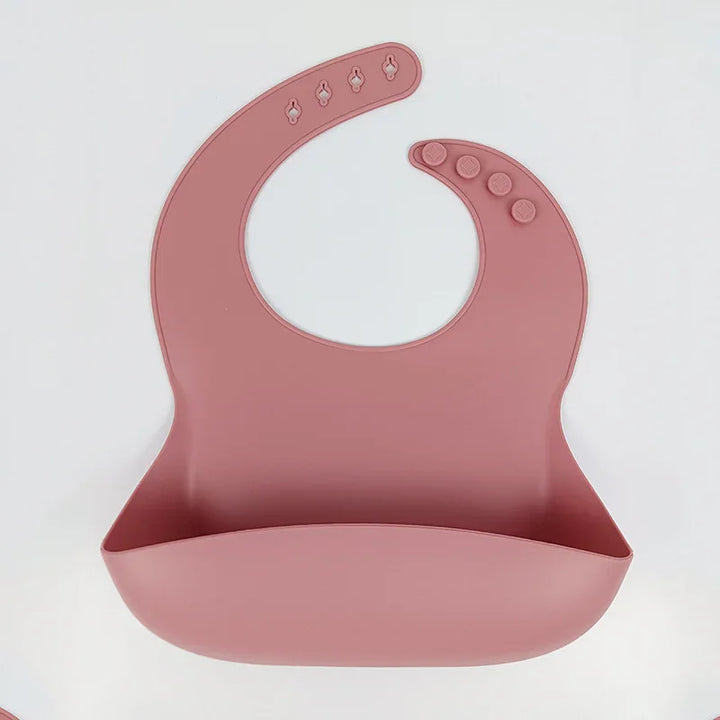 silicone baby bib in muted pink with adjustable button snaps and food catcher pocket