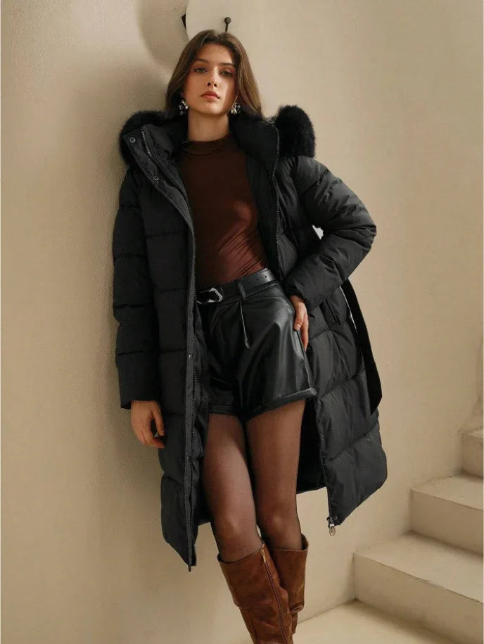 Young woman wearing black puffer coat with fur hood, brown top, leather shorts, and brown boots indoors