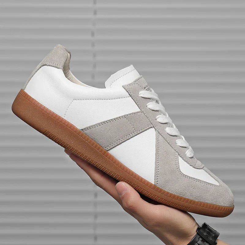 Hand holding white and gray suede leather sneaker with gum sole against gray background