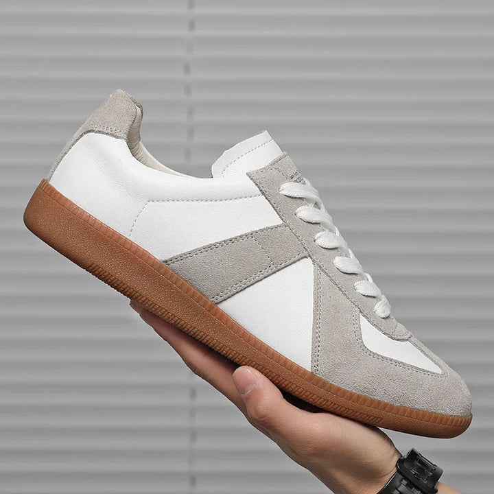 Hand holding white and gray suede leather sneaker with gum sole against gray background