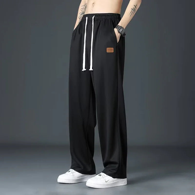 male model wearing black loose-fit pants with white drawstrings and white sneakers on gray background