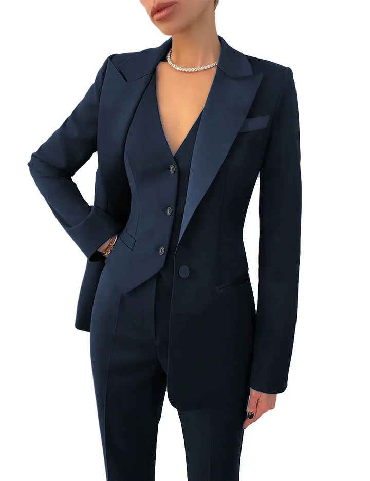 Woman wearing a tailored navy blue suit with blazer, vest, and pants, accessorized with a pearl necklace