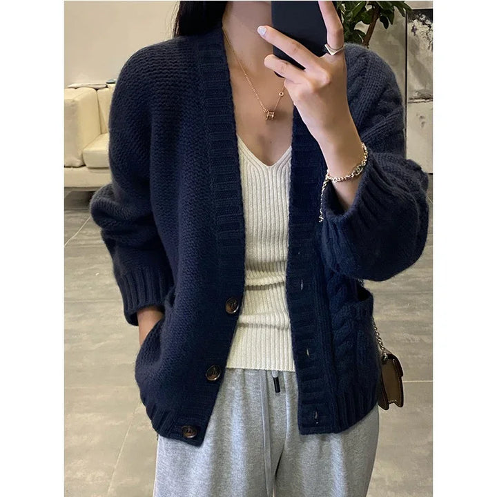 Woman wearing navy blue chunky knit cardigan over white ribbed V-neck top and gray sweatpants
