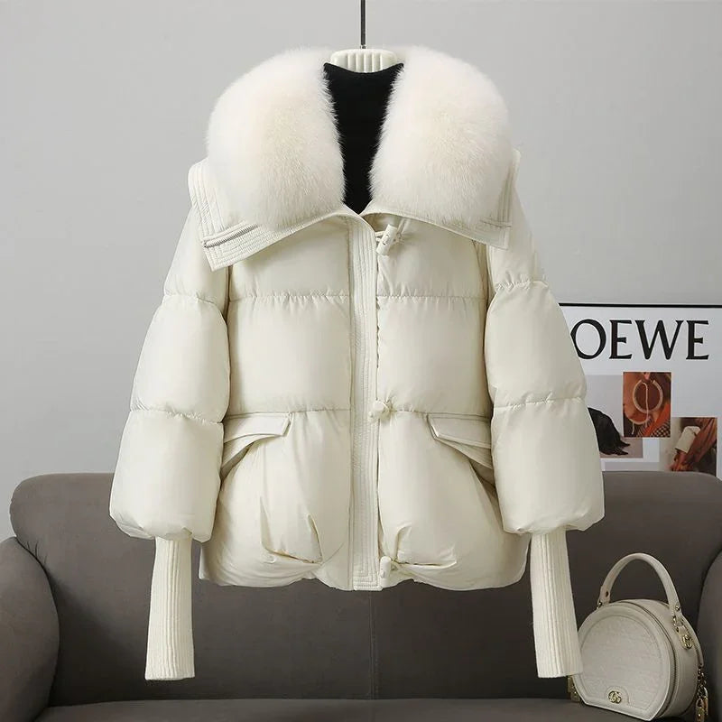 Cream white puffer jacket with large fluffy fur collar hanging on hanger over gray sofa