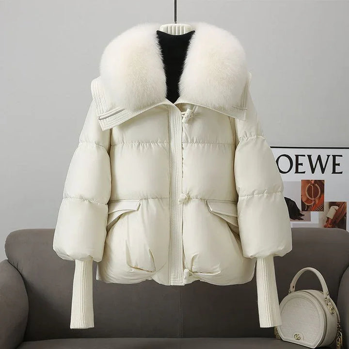 Cream white puffer jacket with large fluffy fur collar hanging on hanger over gray sofa