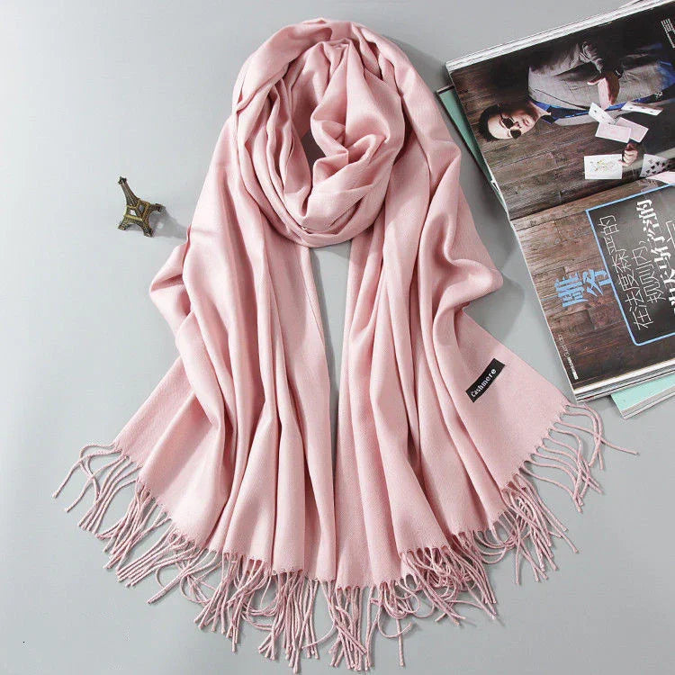 Soft pink cashmere scarf with fringed edges displayed with small Eiffel Tower ornament and magazine