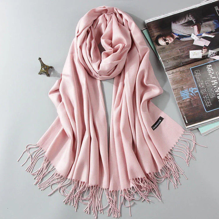 Soft pink cashmere scarf with fringed edges displayed with small Eiffel Tower ornament and magazine