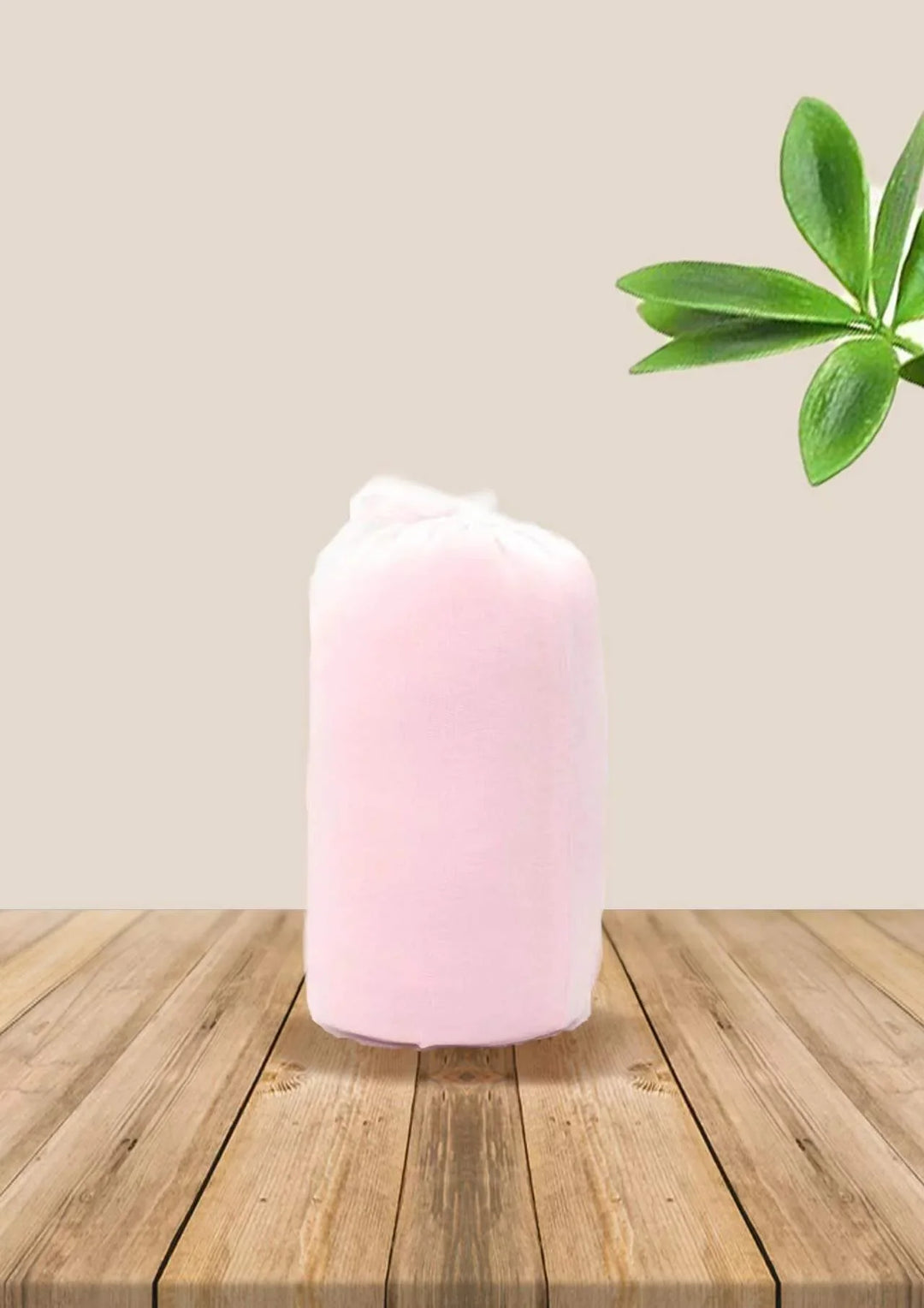 Pink rolled-up towel on wooden surface with green plant leaves on beige background