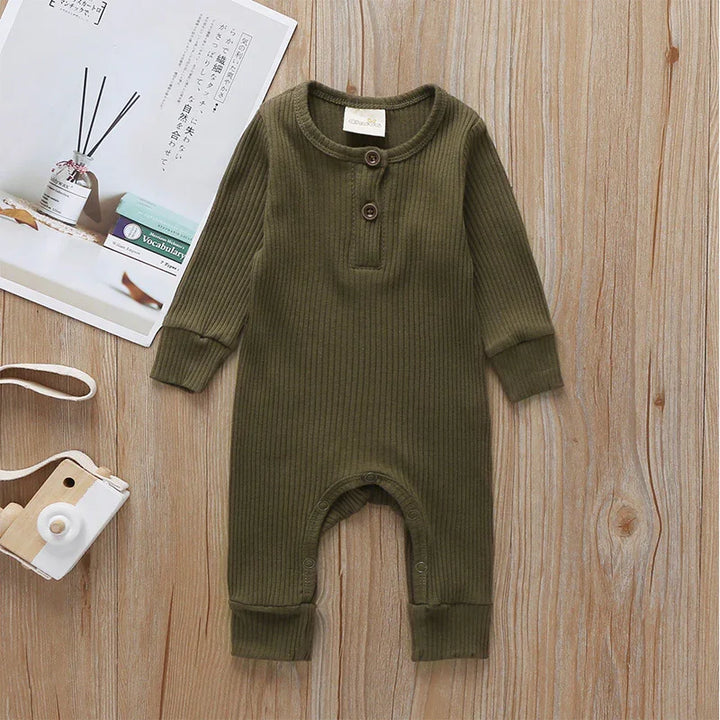 Olive green ribbed baby romper with buttons, displayed on wooden floor alongside wooden toy camera and magazine