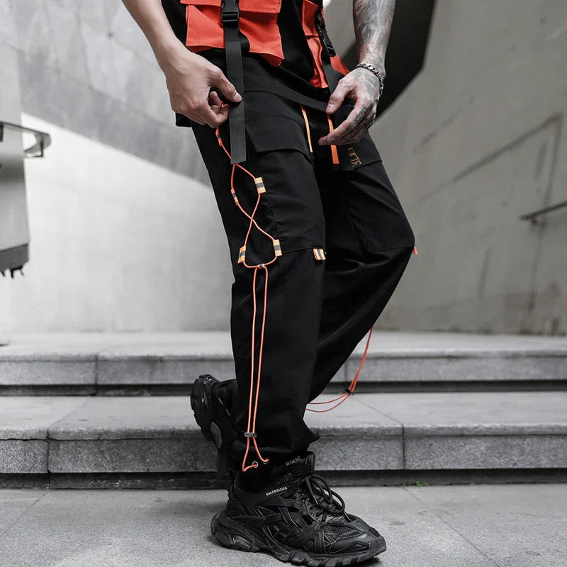 Streetwear style black cargo pants with orange straps and black chunky sneakers on stairs