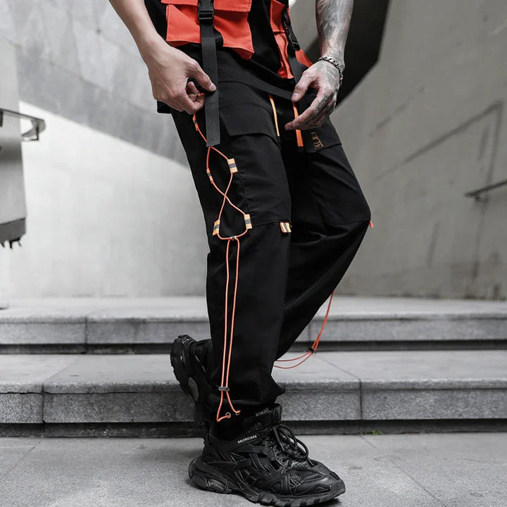 Streetwear style black cargo pants with orange straps and black chunky sneakers on stairs