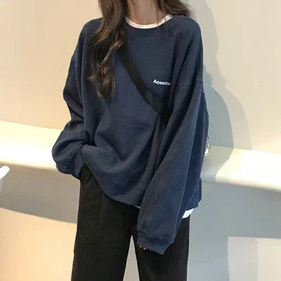 Person wearing oversized navy blue sweatshirt with white and black pants in casual indoor setting